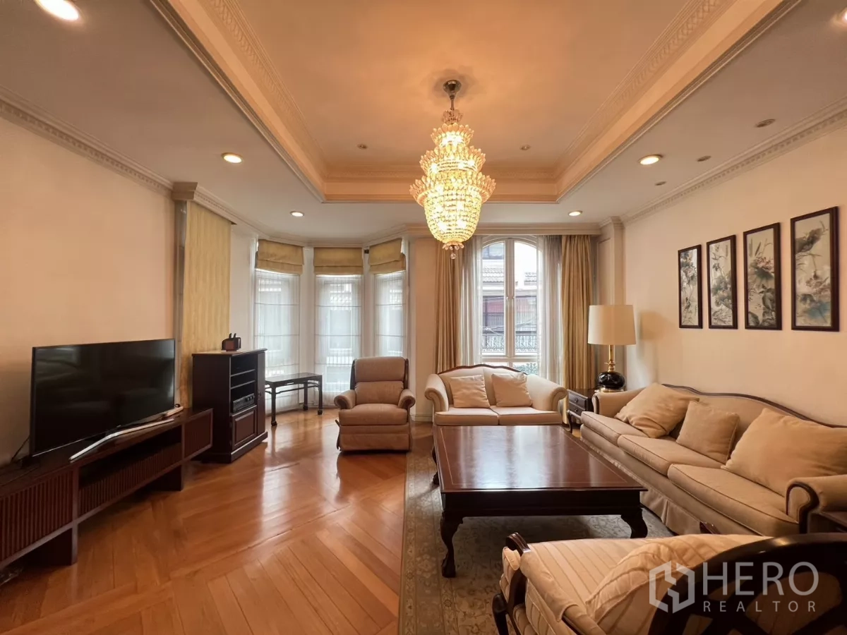 Townhouse for sale in Watthana, Bangkok - Bright living room with chandelier, bay window, cream sofas and warm wood floors.