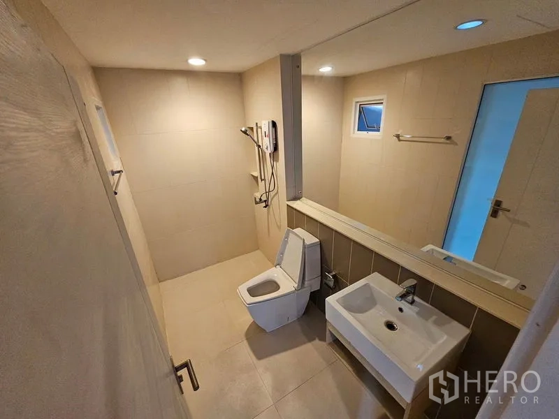 联排别墅 出租在Wang Thonglang, Bangkok - 浅色瓷砖浴室，步入式淋浴、壁挂式洗手盆与坐便器，筒灯照明。