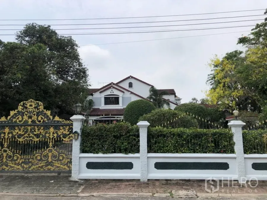 Detached House for rent - Two-storey detached house in Ladawan Srinakarin, Bang Phli with ornate gold gate, white fence and lush landscaped garden.