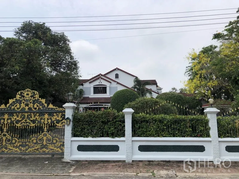 Detached House for rent - Two-storey detached house in Ladawan Srinakarin, Bang Phli with ornate gold gate, white fence and lush landscaped garden.