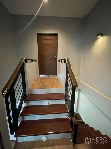 Townhouse for sale in Bang Phli, Samut Prakan - Staircase landing with wooden steps, metal railing and wall light leading to a bedroom door.
