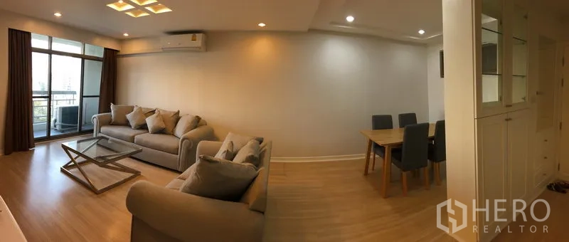 公寓 出租在Watthana, Bangkok - 宽敞客餐厅一体，落地推门通阳台，灰色沙发与四人餐桌。