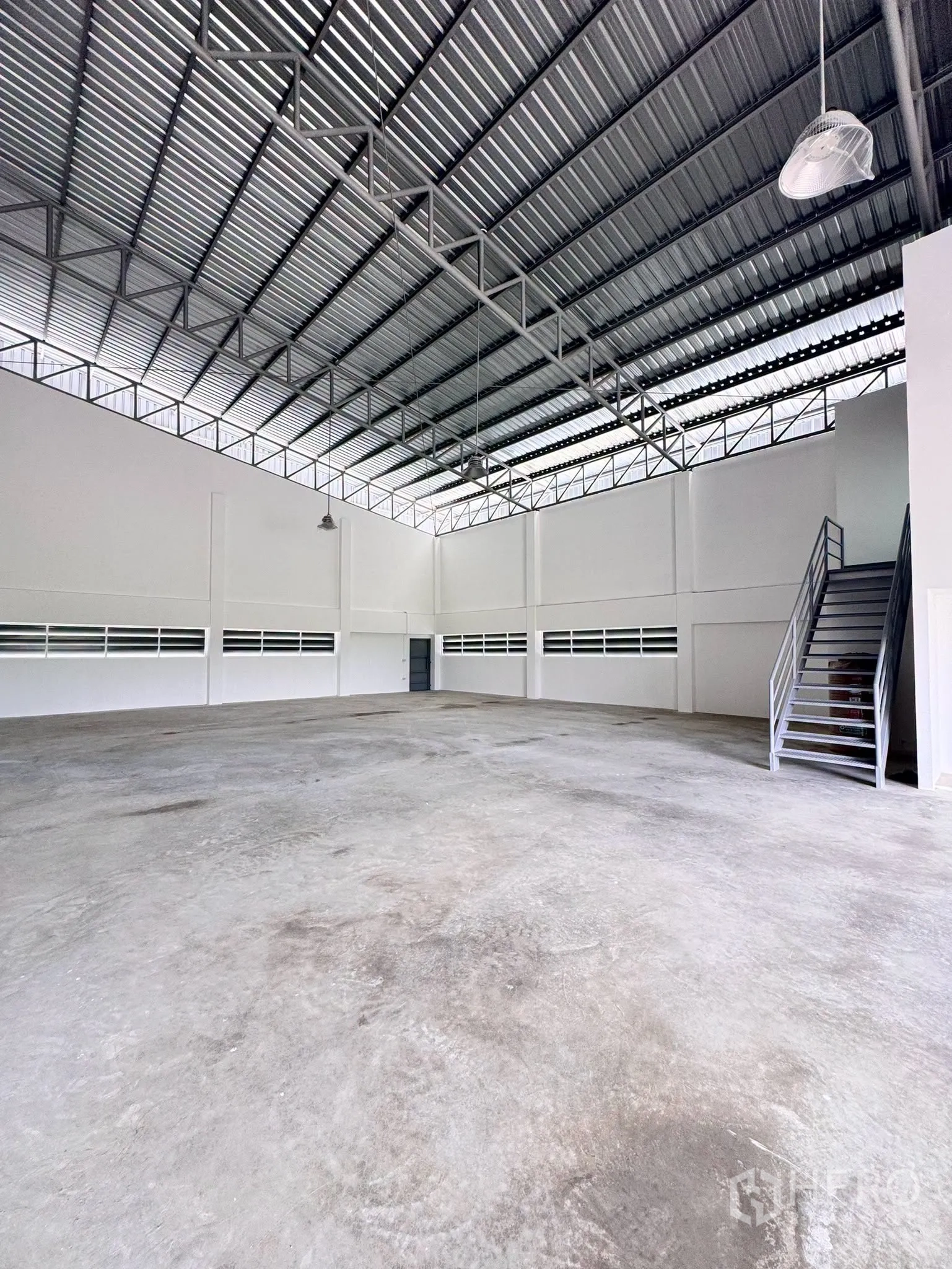Warehouse for rent in Bang Bo, Samut Prakan - Open warehouse hall with concrete floor and hanging lights viewed from another angle.