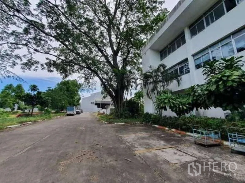 โรงงาน ขายในRayong - ถนนภายในโครงการร่มรื่น ข้างอาคารสำนักงานสีขาวหน้าต่างยาว เชื่อมไปยังพื้นที่คลังสินค้า