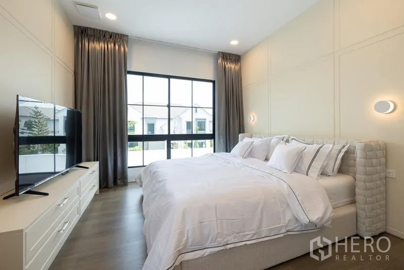 Detached House for sale in Saphan Sung, Bangkok - Bright bedroom with large window, gray curtains, upholstered bed and TV console.