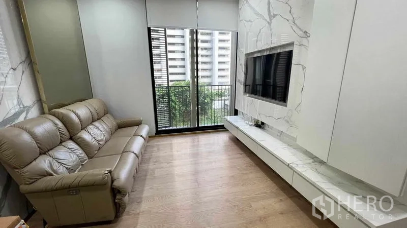 Condominium for rent in Watthana, Bangkok - Living area with marble TV wall and sliding doors to balcony in a Sukhumvit condo.