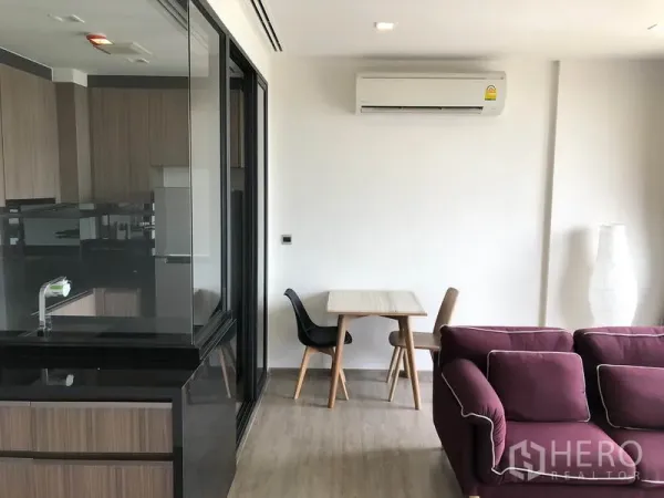 Condominium for rent in Watthana, Bangkok - Compact dining nook beside the glass partition kitchen, with sofa seating and wall air conditioner.