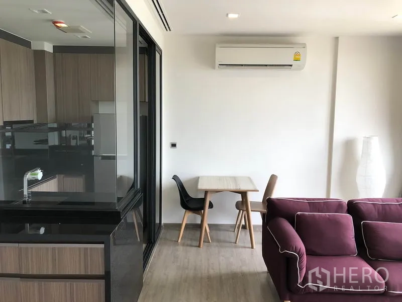 Condominium for rent in Watthana, Bangkok - Compact dining nook beside the glass partition kitchen, with sofa seating and wall air conditioner.