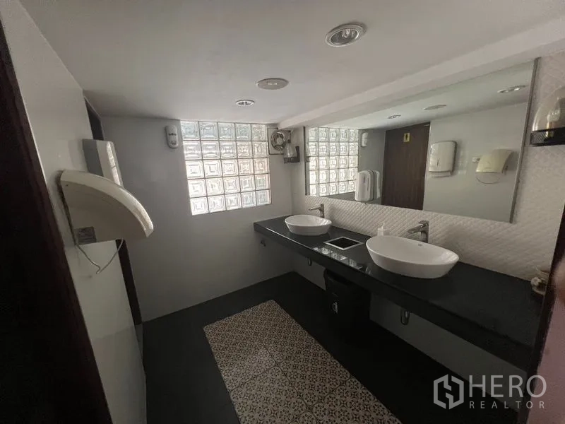 Retail Space for rent or sale in Khlong Toei, Bangkok - Modern restroom with twin basins, long mirror and glass block window.