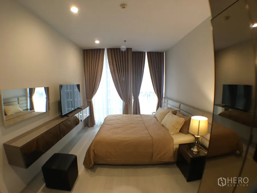 公寓 出租在Pathum Wan, Bangkok - 温馨一居卧室，配大床、电视、落地窗帘与柔和灯光。