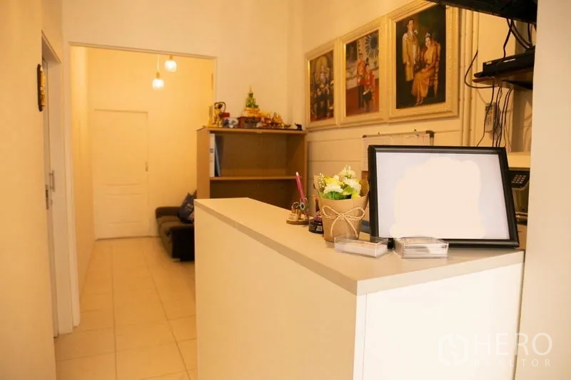 Shophouse for rent in Khlong Toei, Bangkok - Reception area with a white counter, shelving, and framed artwork.