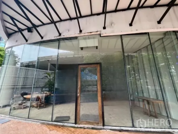 Retail Space for rent - Curved glass-front retail unit with a wooden door under a metal canopy at W District.