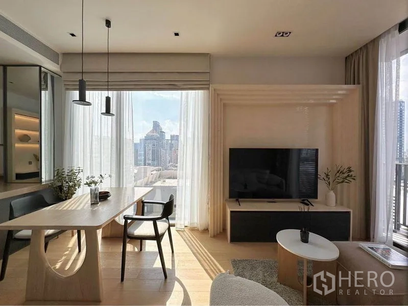 Condominium for rent in Pathum Wan, Bangkok - Bright living and dining area with large windows, city skyline view and a modern TV feature wall.