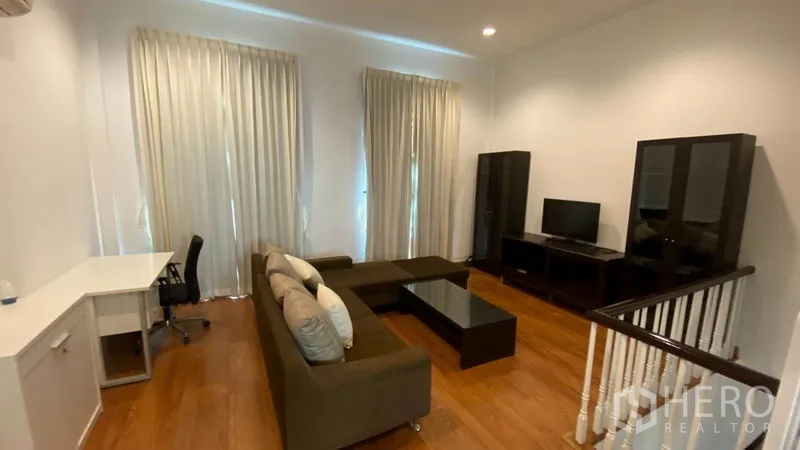 联排别墅 出租在Wang Thonglang, Bangkok - 楼上客厅，转角沙发、电视柜、书桌和高帘。