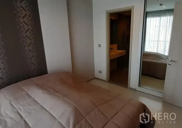 Condominium for rent in Khlong Toei, Bangkok - Cozy bedroom featuring an accent wall, mirrored closet, and entrance to the bathroom.