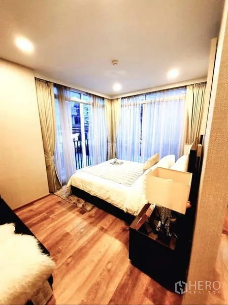 Condominium for sale in Bang Rak, Bangkok - Corner bedroom with bed, wood floors and floor-to-ceiling windows on two sides.