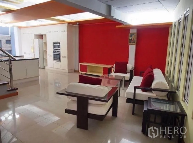 联排别墅 出租在Wang Thonglang, Bangkok - 客厅配白色沙发与红色抱枕，连通开放式厨房与红色特色墙。