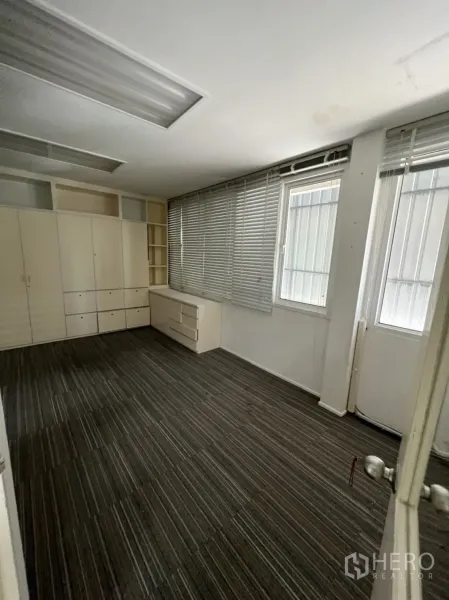 Shophouse for rent or sale in Watthana, Bangkok - Larger carpeted office with built-in cabinets and blinds along the windows.