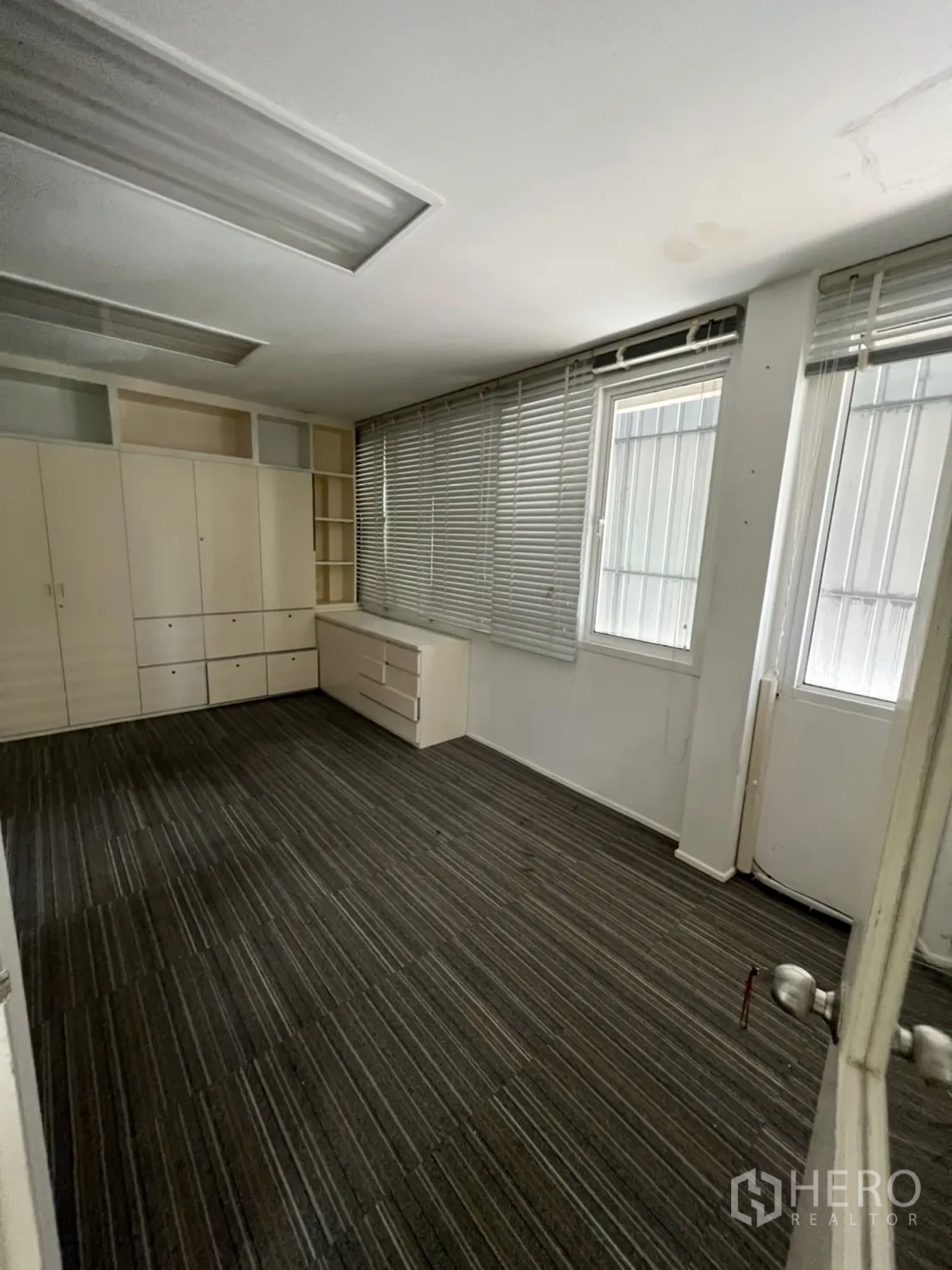 Shophouse for rent or sale in Watthana, Bangkok - Larger carpeted office with built-in cabinets and blinds along the windows.