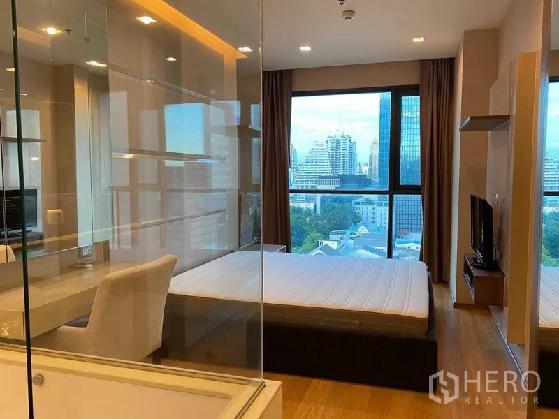 Condominium for rent in Bang Rak, Bangkok - Bedroom with work desk and glass-walled bath facing floor-to-ceiling windows.