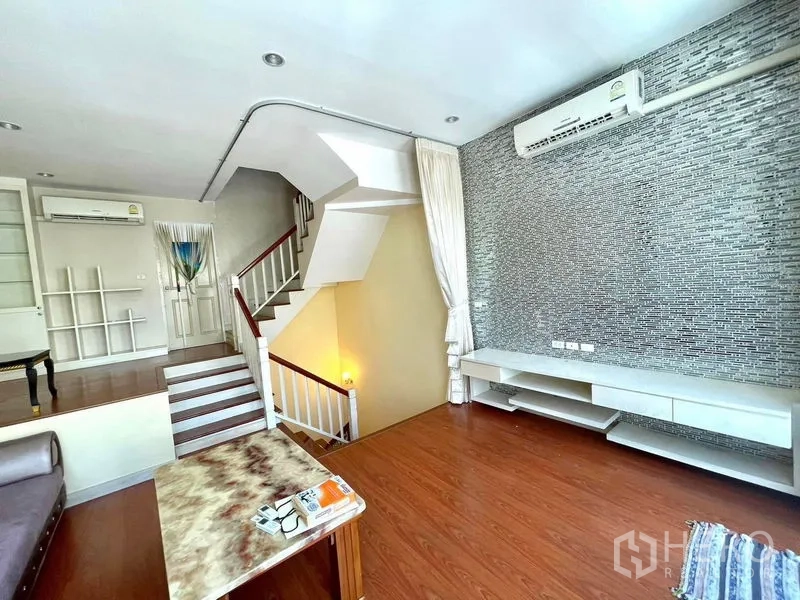 Townhouse for rent in Saphan Sung, Bangkok - Split‑level living room with wood floors, feature stone wall, staircase and built‑in TV shelf.