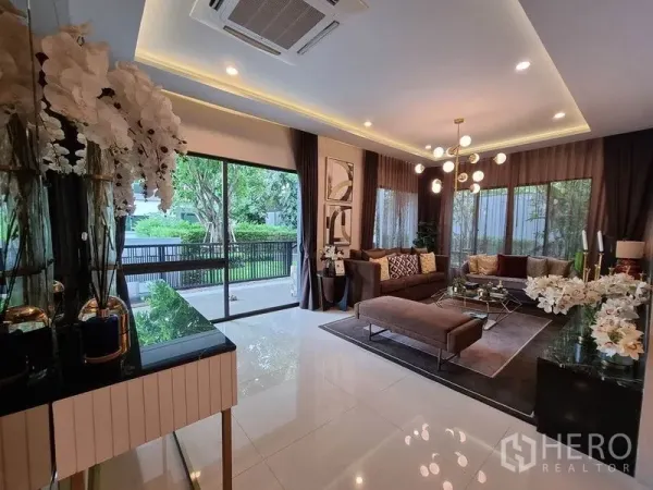 独立式住宅 出租在Prawet, Bangkok - 采光充足的客厅，推拉落地门、造型吊灯与花园景观。