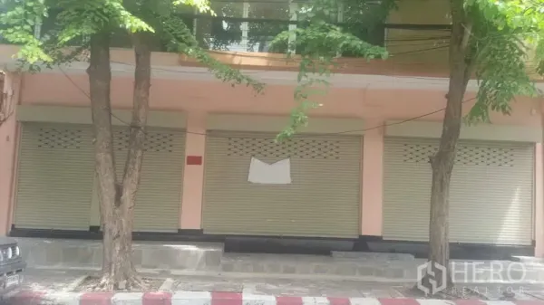 办公空间 出租在Sathon, Bangkok - 沙吞街边建筑外立面，三扇米色卷闸门与行道树成荫。