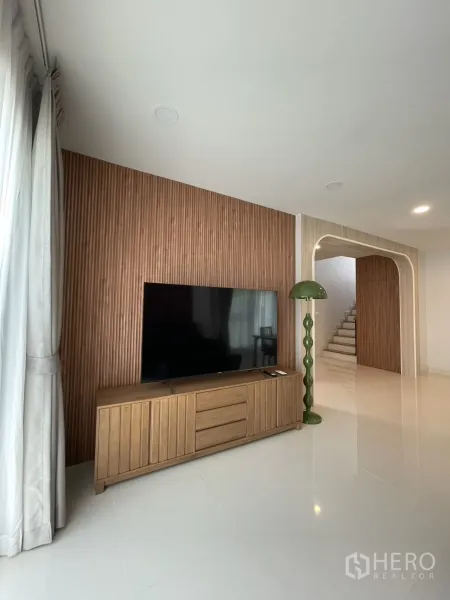 独立式住宅 出租在Bang Phli, Samut Prakan - 客厅木质格栅背景墙，电视与矮柜，拱形门和楼梯，Centro Bangna独立屋。