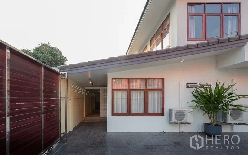 Detached House for sale in Chatuchak, Bangkok - Side courtyard with air-conditioning units, potted plant and red-framed windows.