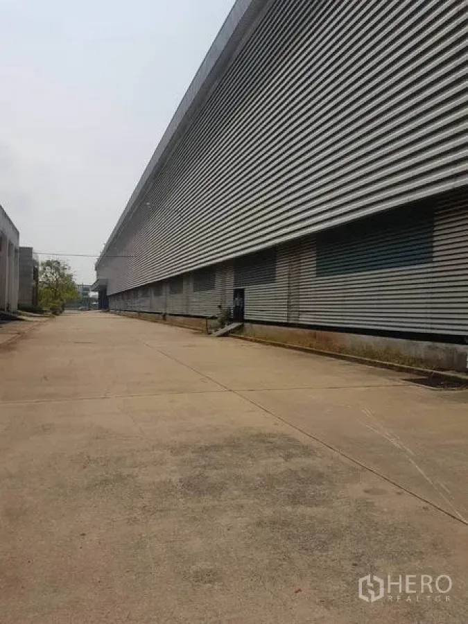 工厂 出租在Mueang Samut Sakhon, Samut Sakhon - 宽阔混凝土车道与长条形金属外墙的工厂外观，设多处装卸区，位于Samut Sakhon。