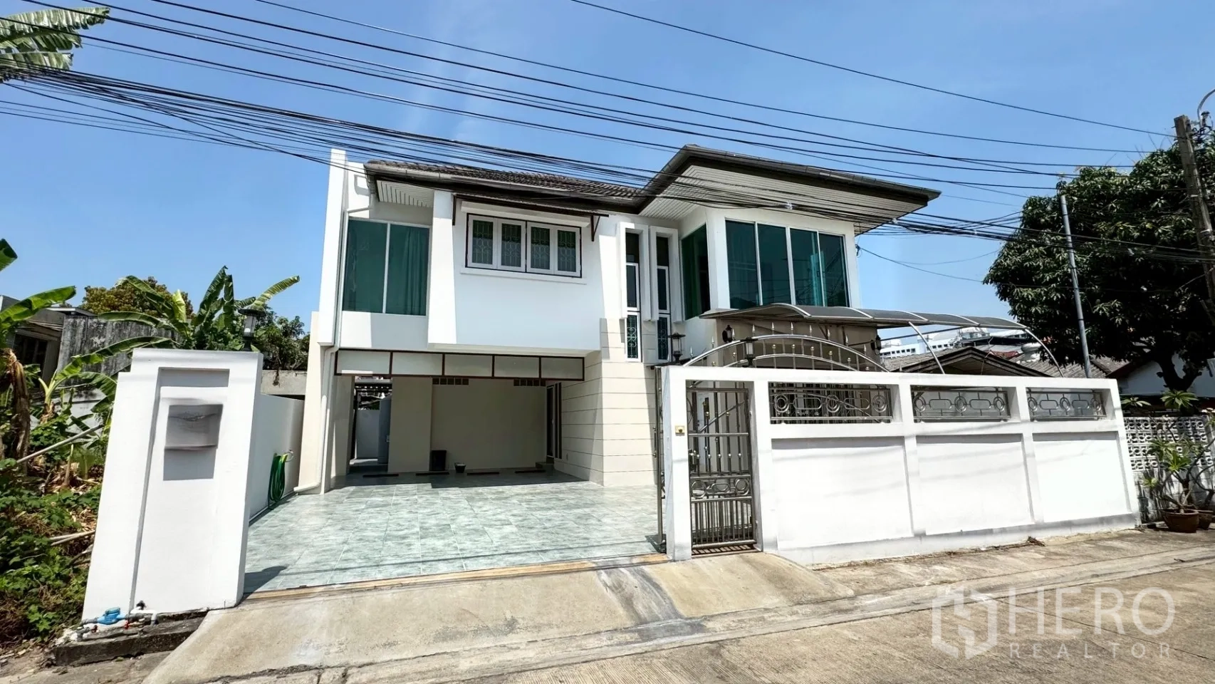 บ้านเดี่ยว for rent in Suan Luang, Bangkok - มุมมองด้านหน้าบ้านเดี่ยวสองชั้นสีขาว มีกำแพงรั้ว ประตูเหล็ก และทางเข้าปูกระเบื้องกว้าง