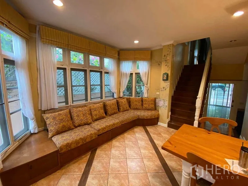 Townhouse for rent or sale in Mueang Samut Prakan, Samut Prakan - Cozy bay-window family area with L-shaped built-in sofa and staircase.