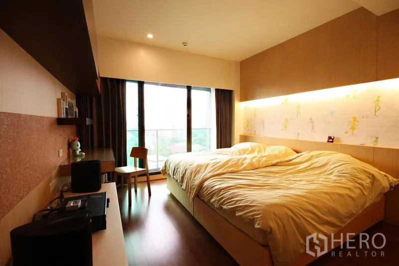 Condominium for rent or sale in Khlong Toei, Bangkok - Master bedroom with large window, built-in headboard lighting, and wood floors.