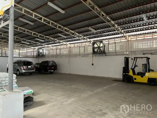 Warehouse for rent in Suan Luang, Bangkok - Wide parking and staging zone with industrial wall fans and a forklift under a ventilated metal roof.
