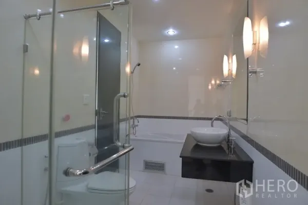 公寓 出租在Ratchathewi, Bangkok - 现代浴室，玻璃淋浴间与浴缸，台上盆搭配墙面照明。