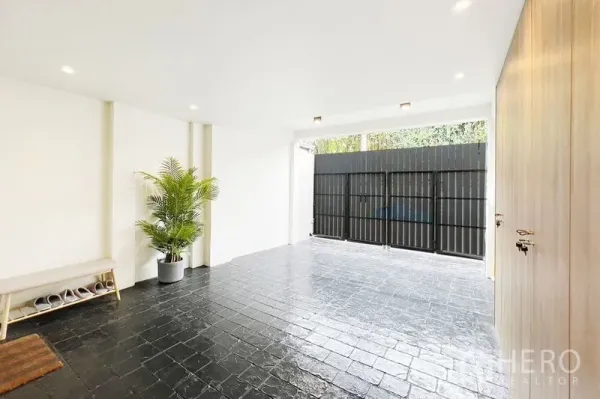 Townhouse for rent in Khlong Toei, Bangkok - Covered carport with black tiled floor, leafy plant, bench and secure metal gate.