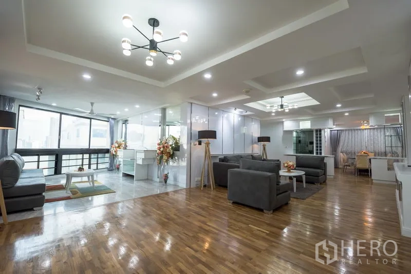 Condominium for rent in Khlong Toei, Bangkok - Open-plan living space with multiple seating areas, floor-to-ceiling windows, hardwood floors and modern lighting.