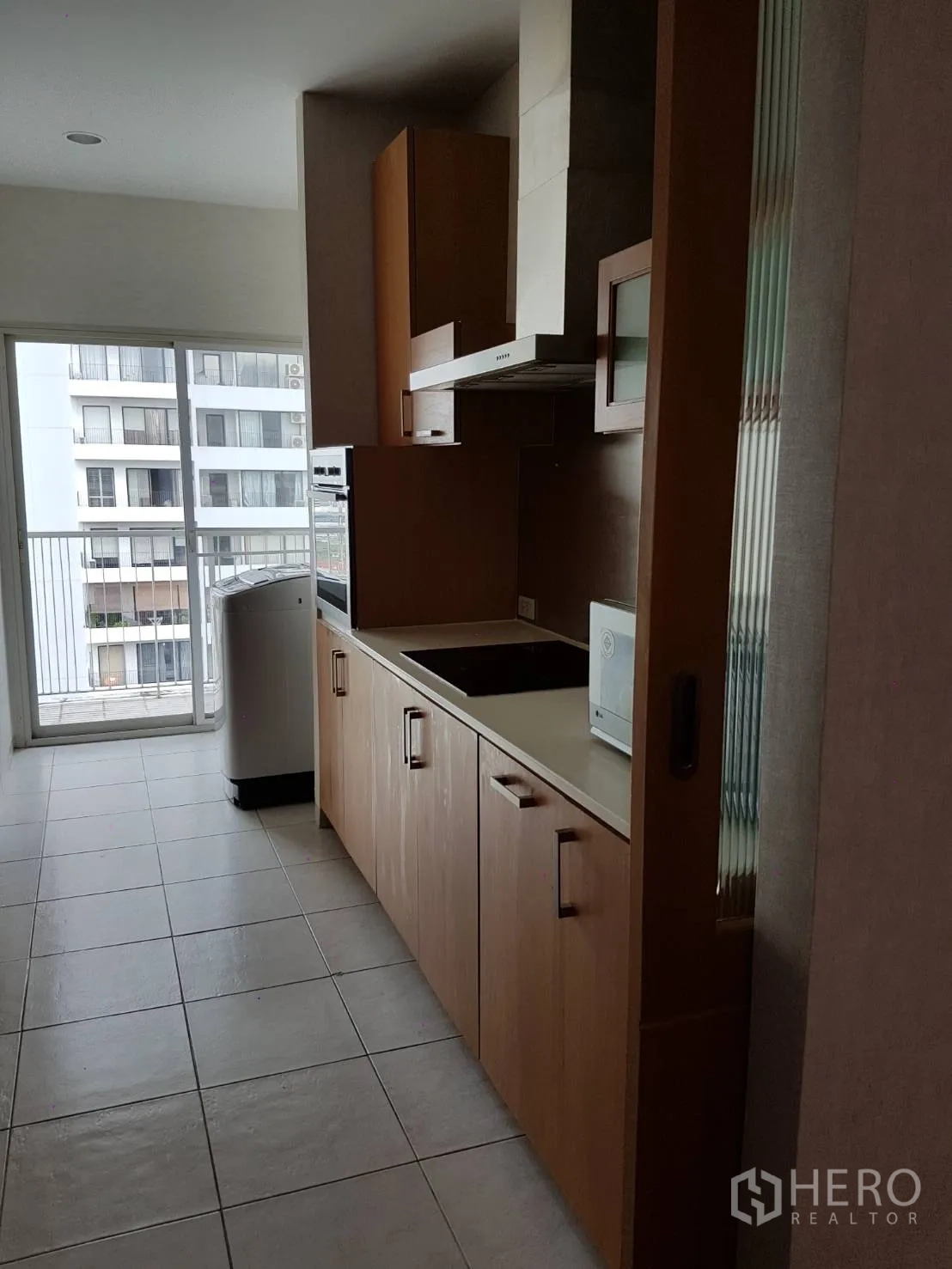公寓 出租或出售在Watthana, Bangkok - 厨房通向阳台，木柜与灶台，推拉门外可见城市景观
