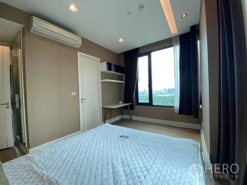 Condominium for rent in Bangkok - Primary bedroom with air-conditioning, desk corner and twin windows framing lush greenery.