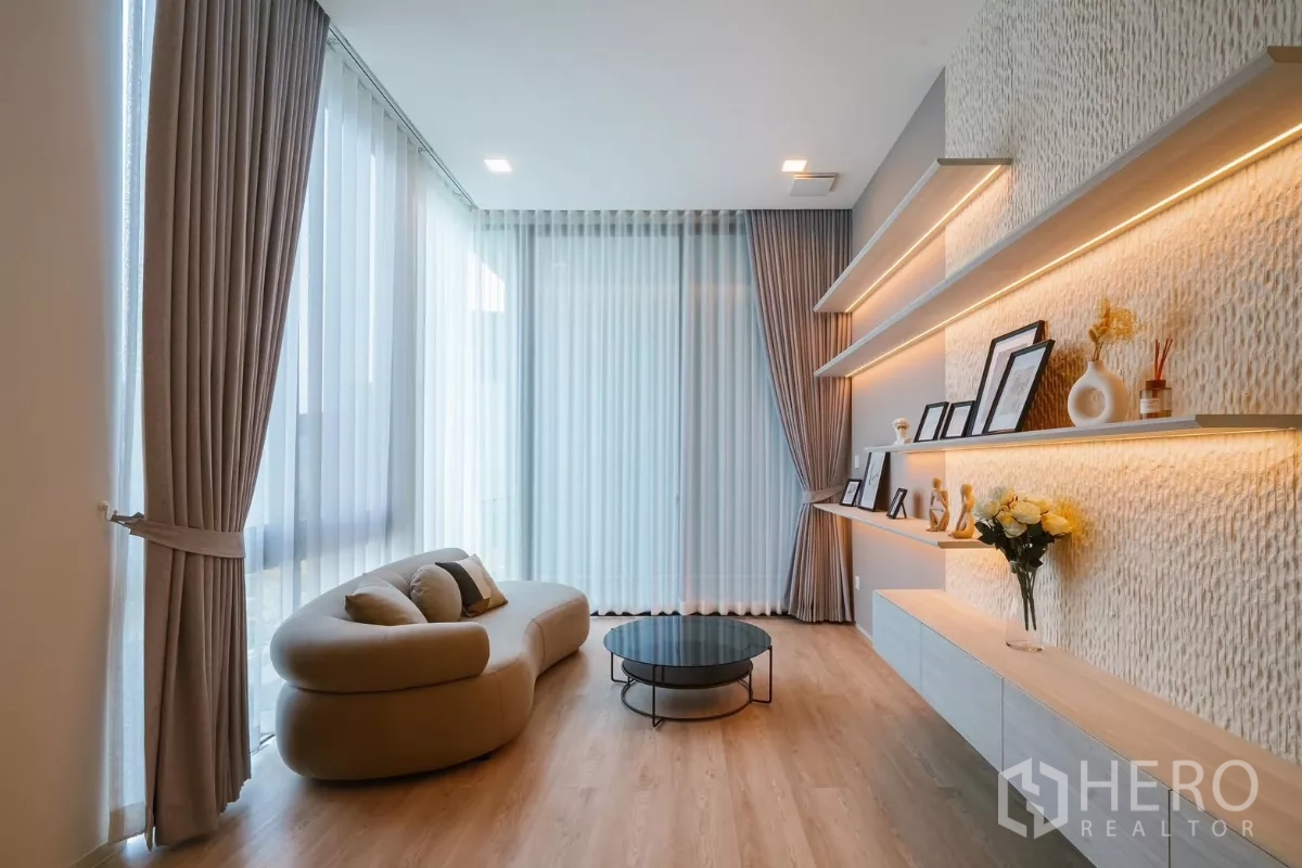 Detached House for rent or sale in Saphan Sung, Bangkok - Sitting lounge with curved sofa, floor-to-ceiling sheer curtains and lit shelves.