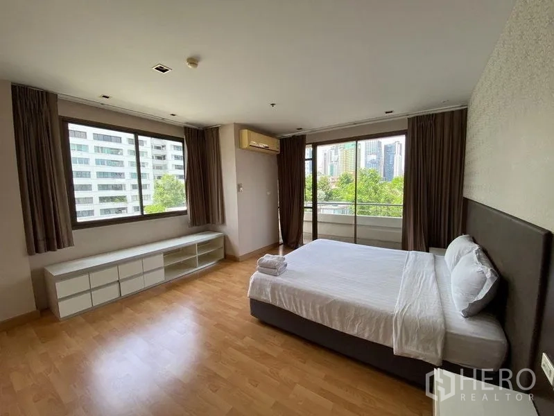 Condominium for rent in Khlong Toei, Bangkok - Spacious bedroom with corner windows, balcony access, and city views.