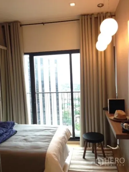 Condominium for rent in Phaya Thai, Bangkok - Cozy bedroom with floor-to-ceiling sliding door to a balcony, draped curtains and globe pendant lights.