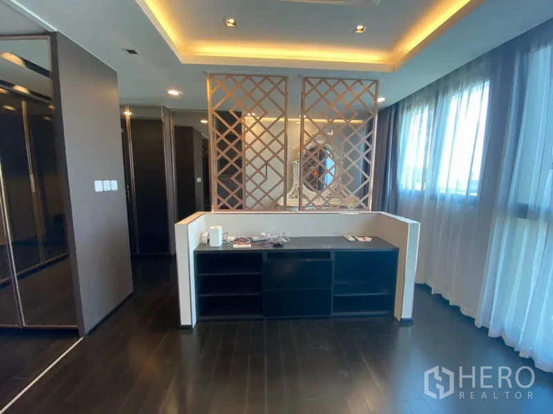 Townhouse for sale in Yan Nawa, Bangkok - Bright bedroom zone with dark wood floors, lattice room divider, ceiling cove lighting and wide curtained windows.
