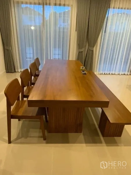 Townhouse for rent in Prawet, Bangkok - Solid wood dining table with chairs and a bench set by full-height curtains.