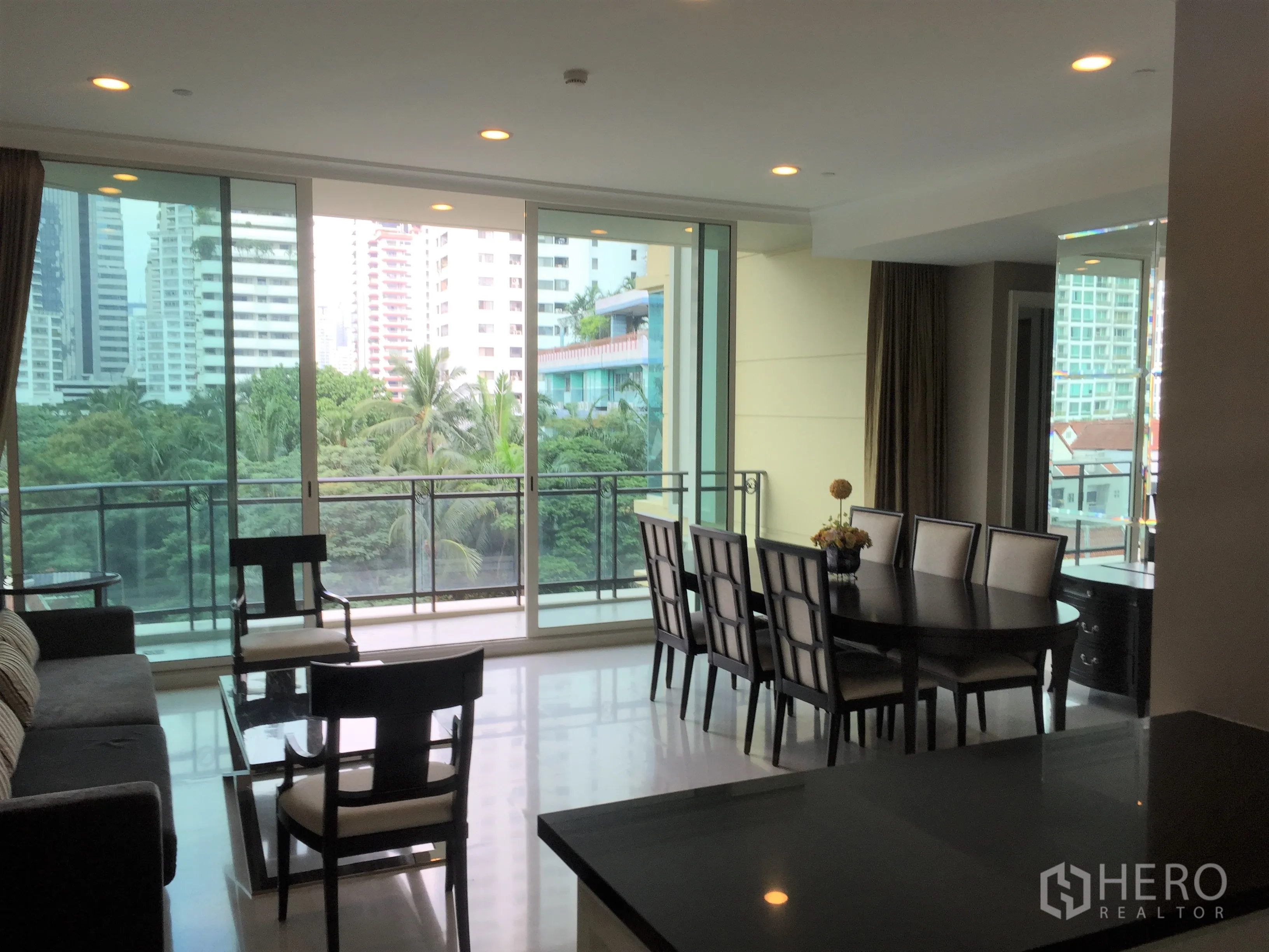 Condominium for rent in Watthana, Bangkok - Open-plan lounge and dining room with floor-to-ceiling windows and greenery outlook.