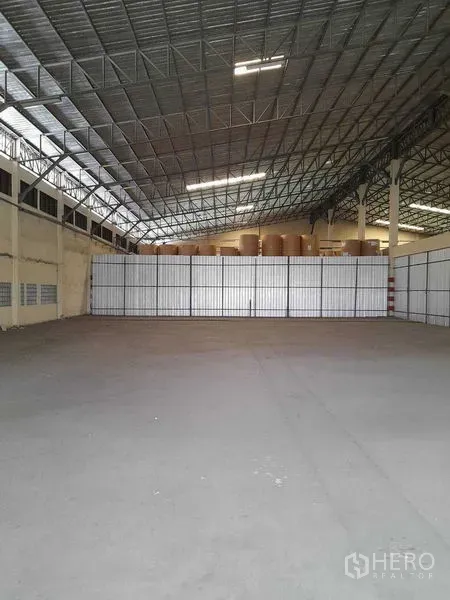 Warehouse for rent in Yan Nawa, Bangkok - Open storage bay facing a tall metal partition wall under bright strip lighting.