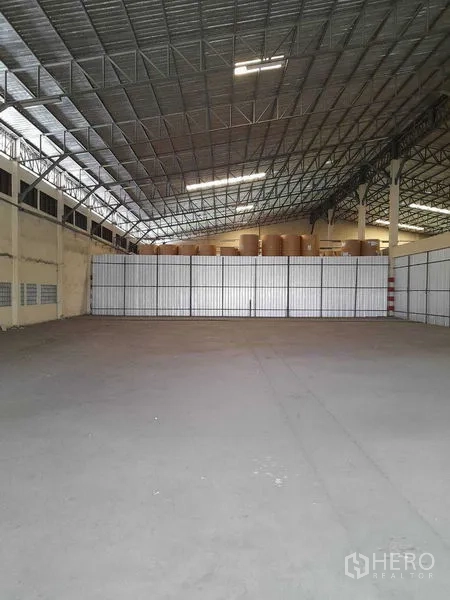 Warehouse for rent in Yan Nawa, Bangkok - Open storage bay facing a tall metal partition wall under bright strip lighting.