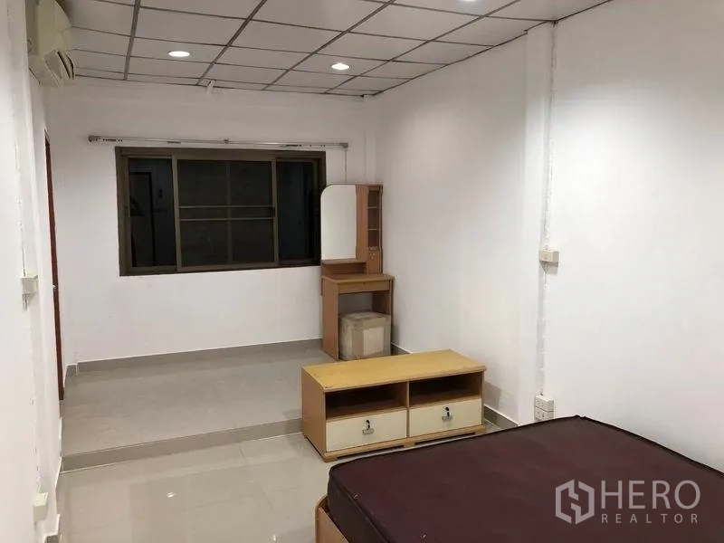 Townhouse for rent in Watthana, Bangkok - Bedroom with window, tiled floor and basic furniture including a dressing table.