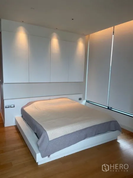 Condominium for rent in Pathum Wan, Bangkok - Primary bedroom with platform bed, wood floors and soft recessed lighting.