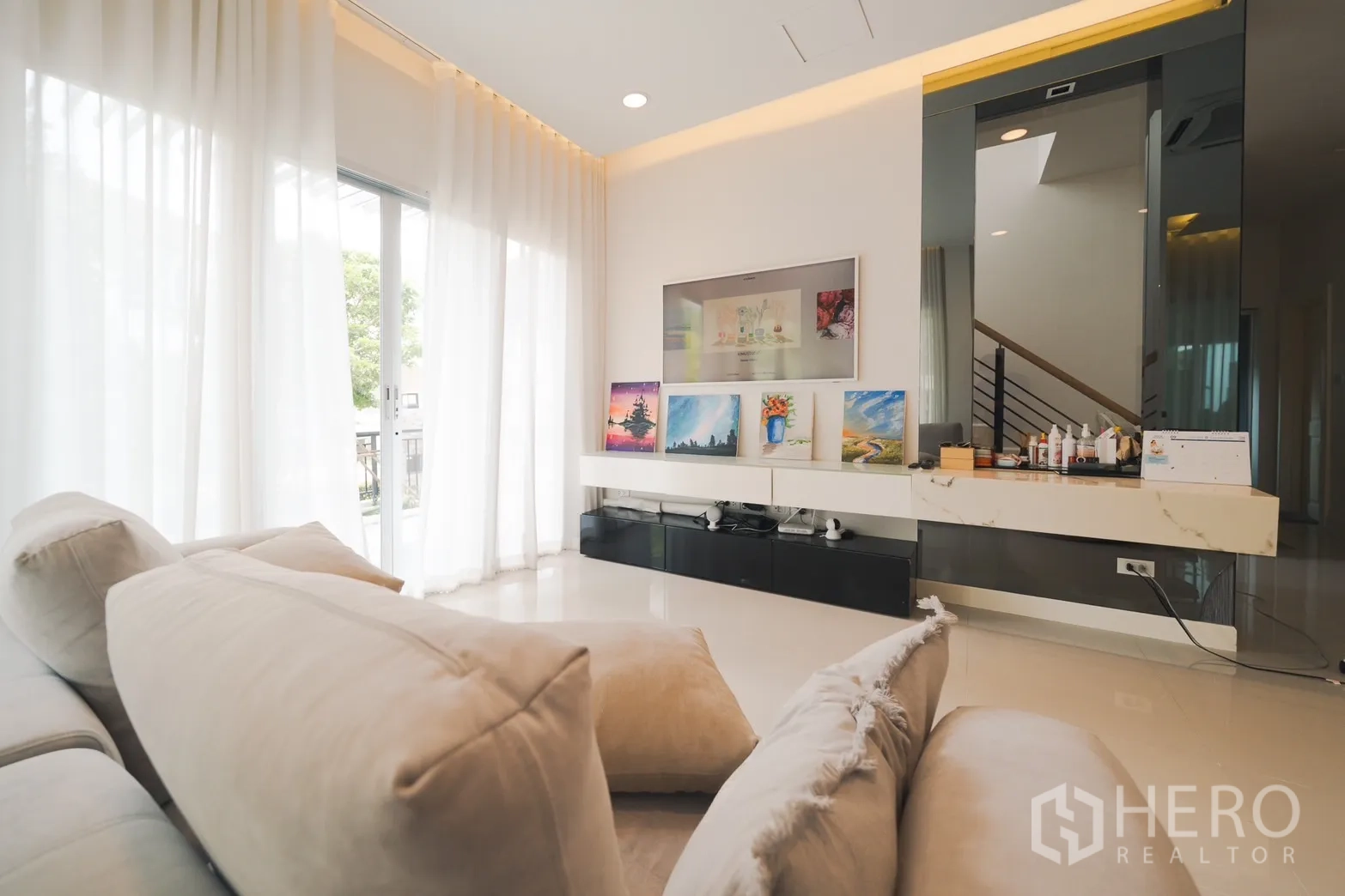 Detached House for rent or sale in Saphan Sung, Bangkok - View from the sofa toward the TV wall and stairwell with a glossy partition and LED cove lighting.